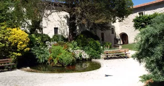Bâtiments en pierre entourant le jardin, bassin encadré par des banc, espace très végétalisé