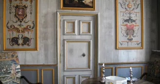 Salle avec murs boisés et peintures, fauteuil et table ornée de bougie