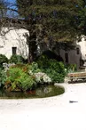 Bâtiments en pierre entourant le jardin, bassin encadré par des banc, espace très végétalisé