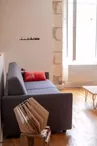 Salon avec mur en pierre, canapé-lit, chaise en osier et télévision